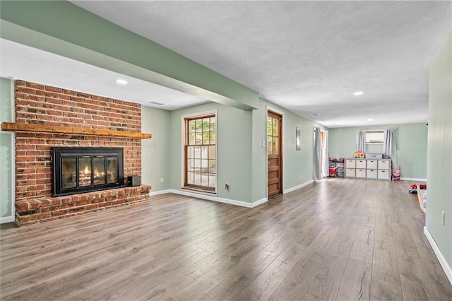 unfurnished living room with hardwood / wood-style floors, a fireplace, baseboards, a textured ceiling, and recessed lighting