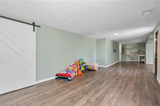 game room featuring a barn door, wood finished floors, baseboards, and a textured ceiling