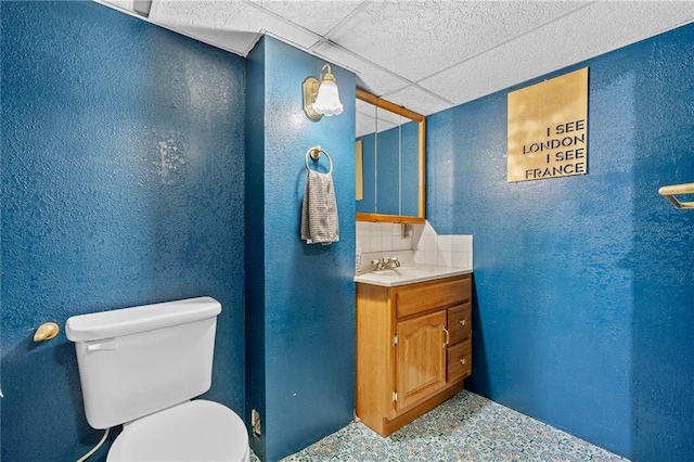 half bathroom featuring a textured wall, toilet, and vanity