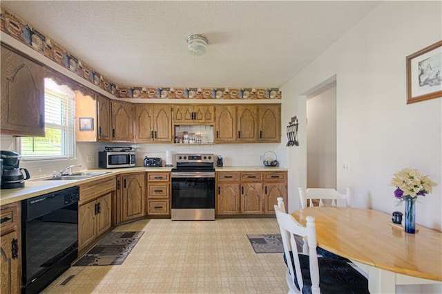 kitchen featuring stainless steel appliances, a sink, brown cabinetry, light countertops, and light floors