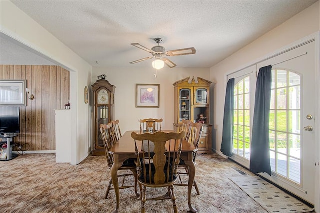 dining area with light carpet, wooden walls, a textured ceiling, a ceiling fan, and baseboards