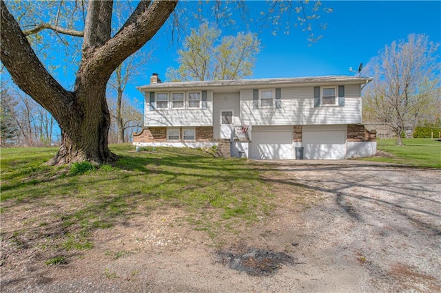 raised ranch featuring a garage, a chimney, a front lawn, driveway, and brick siding