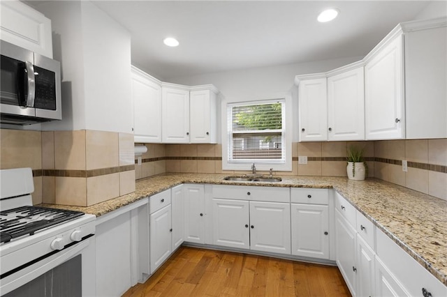 805 N 18th St, Kansas City, KS 66102 - kitchen with white gas range oven, stainless steel microwave, a sink, light wood-style floors, and white cabinets