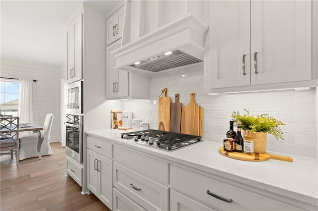8016 Round Prairie St, Shawnee, KS 66220 - kitchen with wood finished floors, decorative backsplash, stainless steel appliances, custom range hood, and white cabinetry