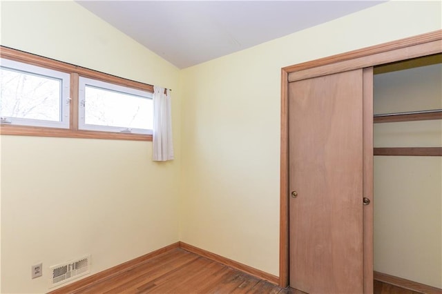 unfurnished bedroom featuring a closet, baseboards, visible vents, lofted ceiling, and wood finished floors