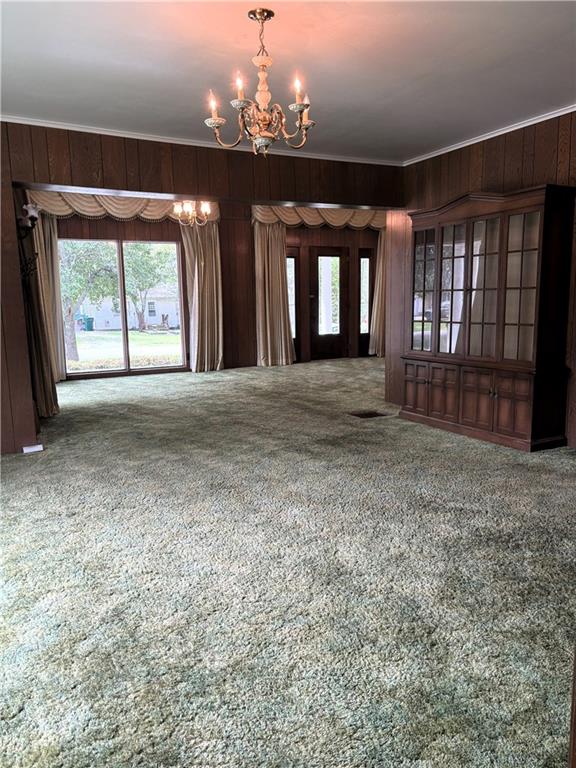 214 W 5th St, Lebo, KS 66856 - unfurnished living room featuring a chandelier, carpet floors, wooden walls, healthy amount of natural light, and crown molding