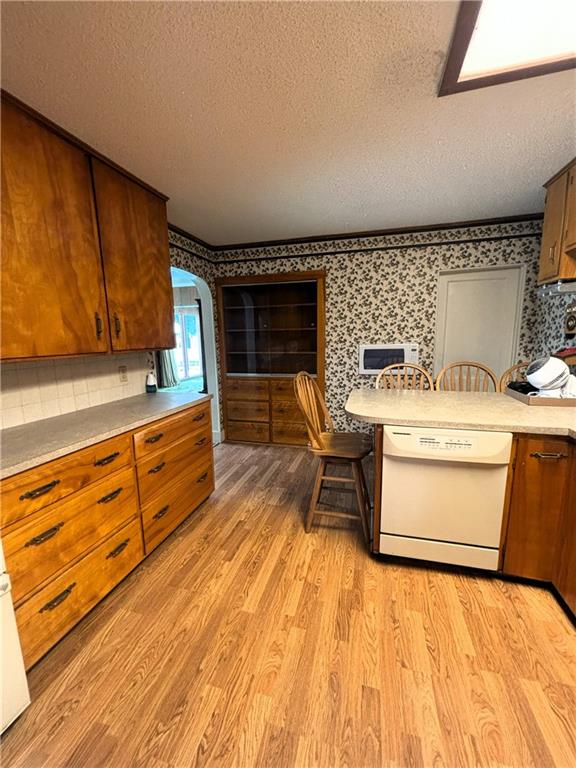214 W 5th St, Lebo, KS 66856 - kitchen featuring wallpapered walls, a textured ceiling, dishwasher, light wood finished floors, and brown cabinets