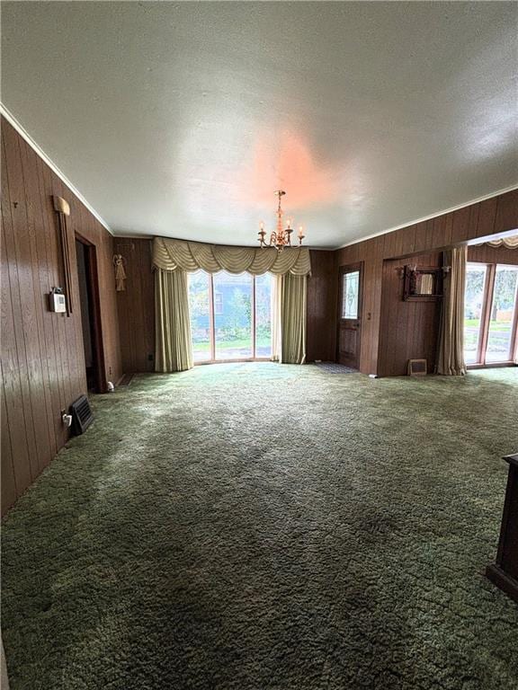 214 W 5th St, Lebo, KS 66856 - unfurnished living room featuring wood walls, a chandelier, carpet floors, healthy amount of natural light, and a textured ceiling