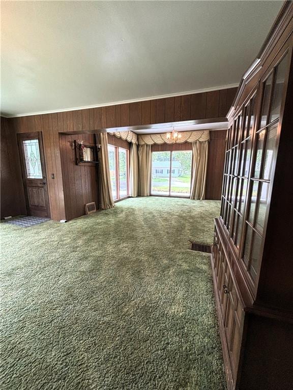 214 W 5th St, Lebo, KS 66856 - unfurnished living room with a chandelier, carpet flooring, wooden walls, and healthy amount of natural light