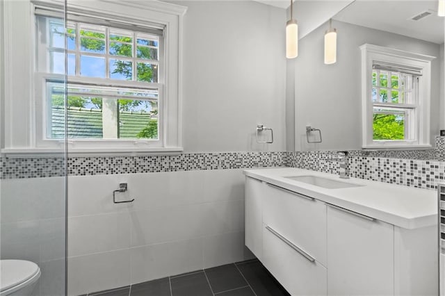 4525 Kenwood Ave, Kansas City, MO 64110 - bathroom with tiled shower, vanity, toilet, tile walls, and tile patterned floors