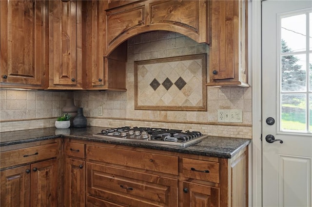 9015 Craig Dr, De Soto, KS 66018 - kitchen with stainless steel gas stovetop, brown cabinetry, decorative backsplash, and dark stone counters