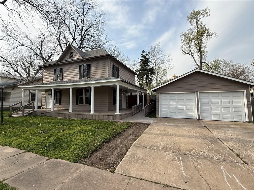 706 E Jackson Ave, Iola, KS 66749 - farmhouse with an outbuilding, a porch, a front lawn, and a detached garage