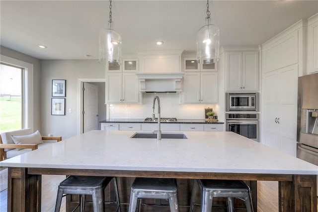 kitchen with decorative light fixtures, white cabinetry, decorative backsplash, a kitchen island with sink, and appliances with stainless steel finishes
