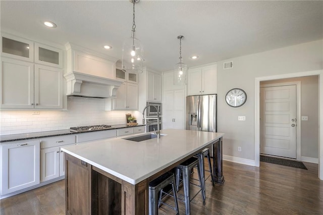 kitchen with baseboards, visible vents, decorative backsplash, a kitchen island with sink, and appliances with stainless steel finishes