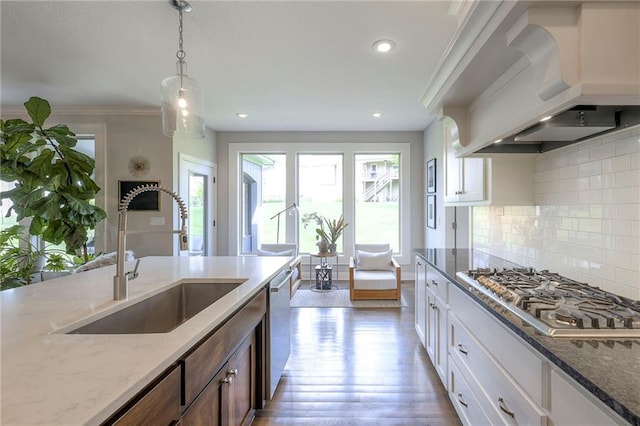 kitchen with a sink, light stone counters, custom range hood, and appliances with stainless steel finishes