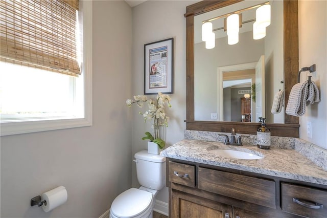 half bathroom with vanity, toilet, and baseboards