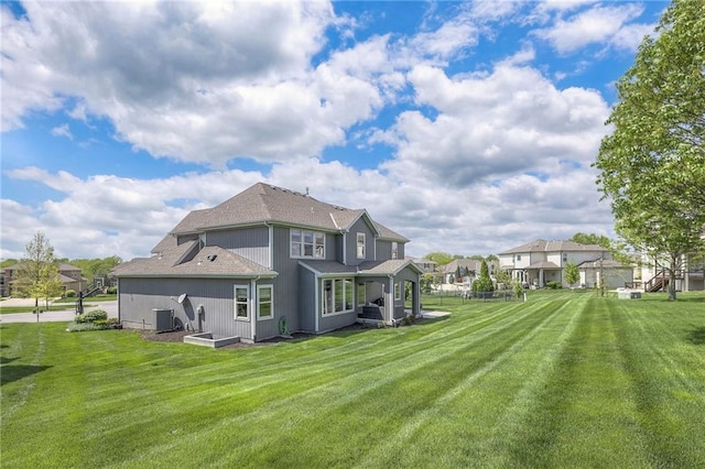 back of property with a yard, roof with shingles, and central AC unit