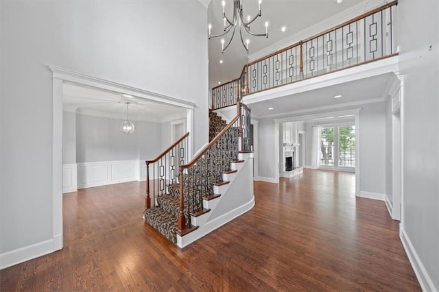 staircase with crown molding, a towering ceiling, a fireplace with raised hearth, and a notable chandelier