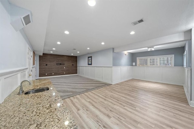 interior space featuring visible vents, a decorative wall, a wainscoted wall, a sink, and light wood-style flooring