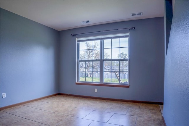 empty room featuring visible vents, baseboards, tile patterned flooring, and a textured wall