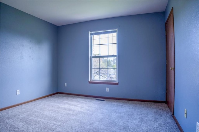 carpeted empty room featuring a healthy amount of sunlight, baseboards, and visible vents