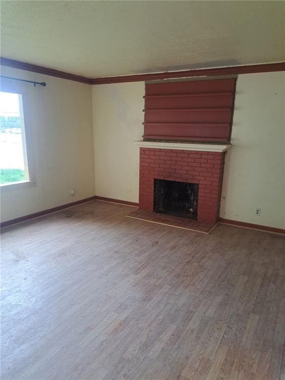 unfurnished living room with crown molding, a brick fireplace, baseboards, and wood finished floors