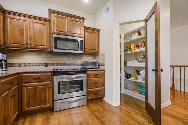 21287 W 116th St, Olathe, KS 66061 - kitchen featuring appliances with stainless steel finishes, light wood finished floors, ornamental molding, backsplash, and stone countertops