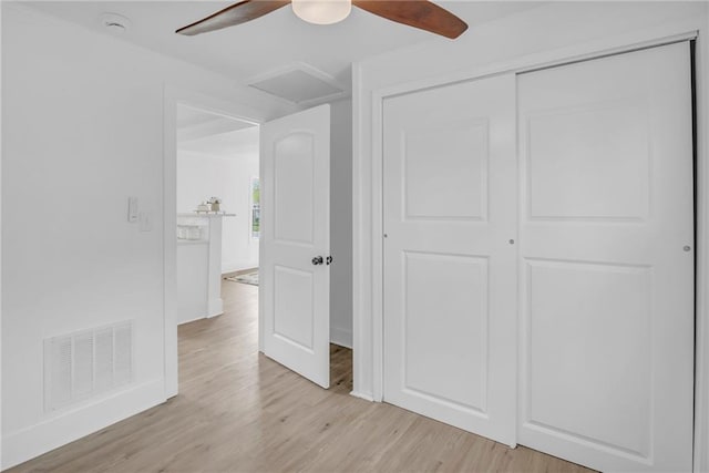 unfurnished bedroom featuring a closet, light wood-type flooring, attic access, visible vents, and ceiling fan