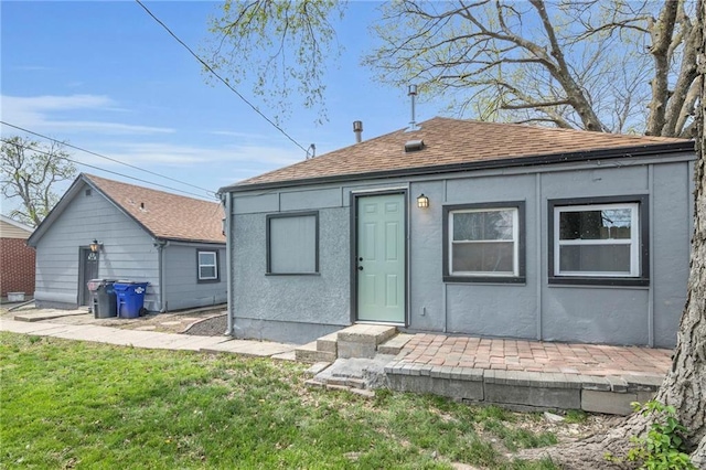 back of house featuring a shingled roof, stucco siding, and a lawn
