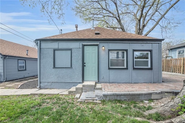 view of front of property featuring stucco siding, fence, and a shingled roof