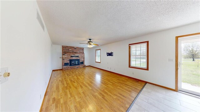 unfurnished living room featuring a fireplace, ceiling fan, visible vents, light wood-style flooring, and a textured ceiling