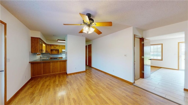 unfurnished living room featuring baseboards, a sink, ceiling fan, and light wood-style floors