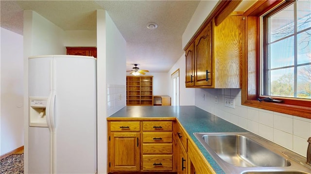 kitchen with brown cabinetry, a textured ceiling, white refrigerator with ice dispenser, and a sink