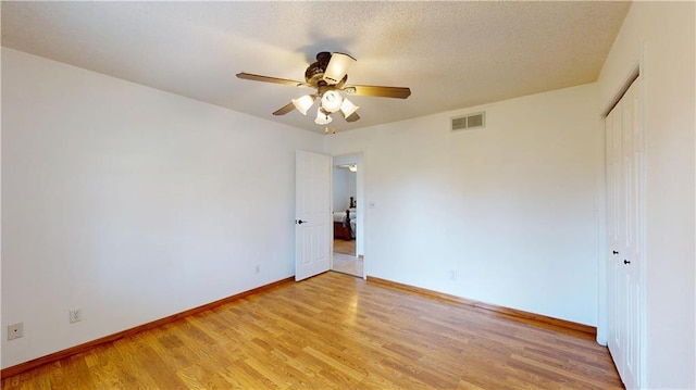 empty room featuring visible vents, a ceiling fan, light wood finished floors, and baseboards