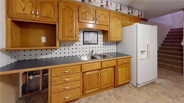 kitchen with brown cabinets, dark countertops, a sink, and white fridge with ice dispenser