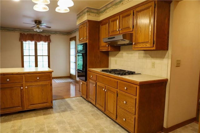 1203 E Quincy St, Pittsburg, KS 66762 - kitchen with stainless steel gas stovetop, under cabinet range hood, light countertops, brown cabinetry, and ceiling fan with notable chandelier