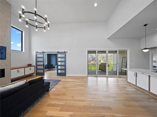 living room featuring a large fireplace, a barn door, baseboards, a chandelier, and light wood-style floors
