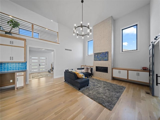living area featuring visible vents, an inviting chandelier, stairs, light wood-style floors, and a large fireplace
