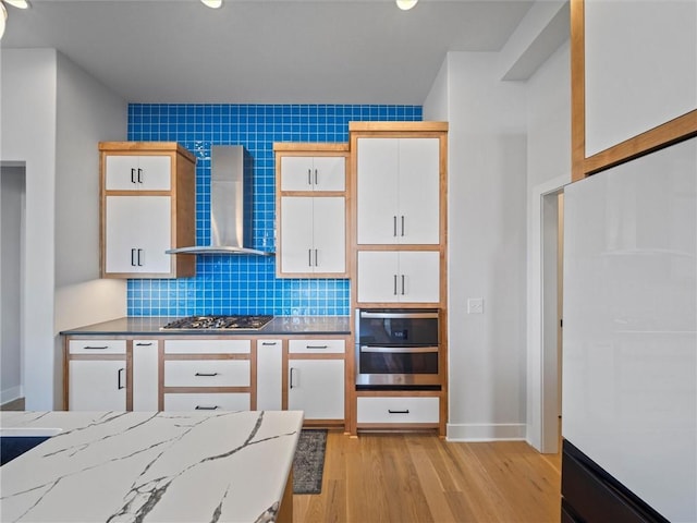 kitchen featuring tasteful backsplash, stainless steel gas cooktop, white cabinetry, light wood-style floors, and wall chimney exhaust hood