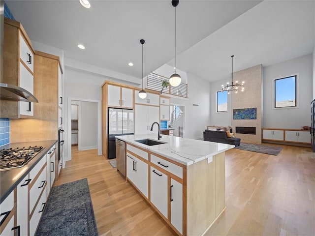kitchen with stainless steel dishwasher, wall chimney range hood, gas stovetop, a sink, and light wood-style flooring