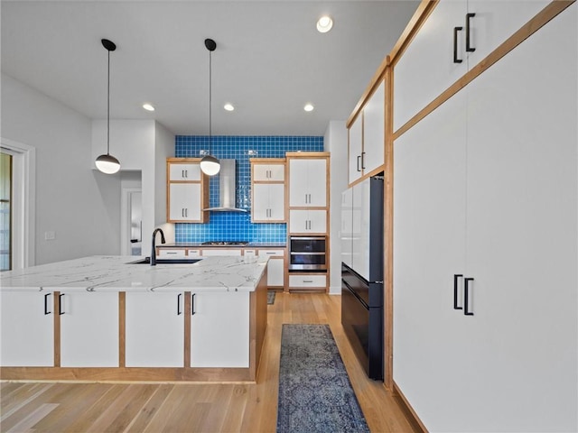 kitchen with light wood-type flooring, wall chimney exhaust hood, a sink, appliances with stainless steel finishes, and backsplash