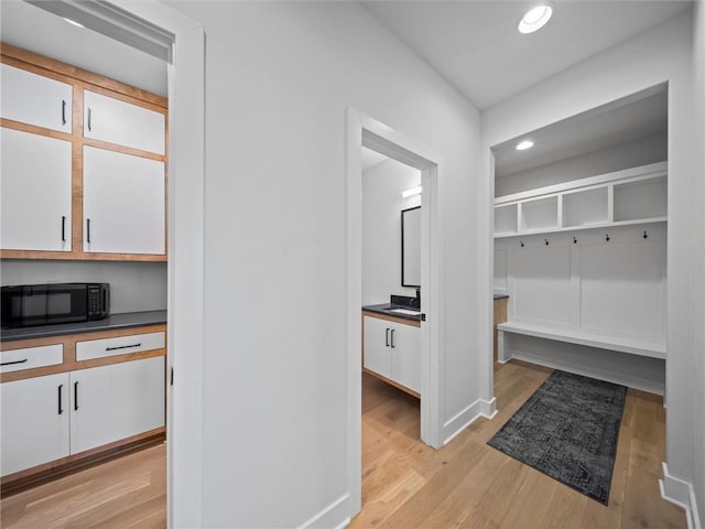 mudroom featuring recessed lighting, a sink, light wood-style flooring, and baseboards