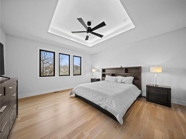 bedroom with light wood-style floors, a ceiling fan, a raised ceiling, and baseboards