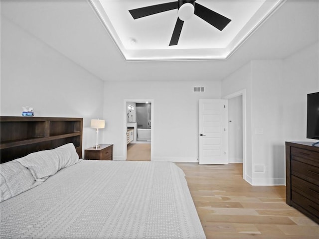 bedroom featuring visible vents, light wood-style flooring, baseboards, and a tray ceiling