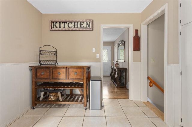 corridor featuring wainscoting, an upstairs landing, and light tile patterned floors