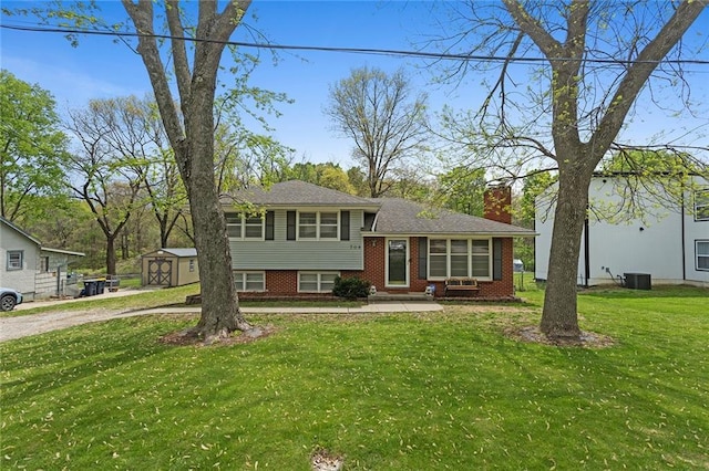 tri-level home with a chimney, a front lawn, central AC, a storage unit, and brick siding