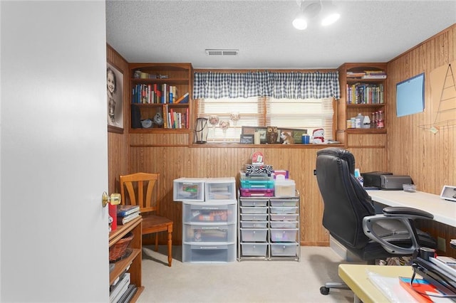 office featuring wooden walls, carpet floors, visible vents, and a textured ceiling