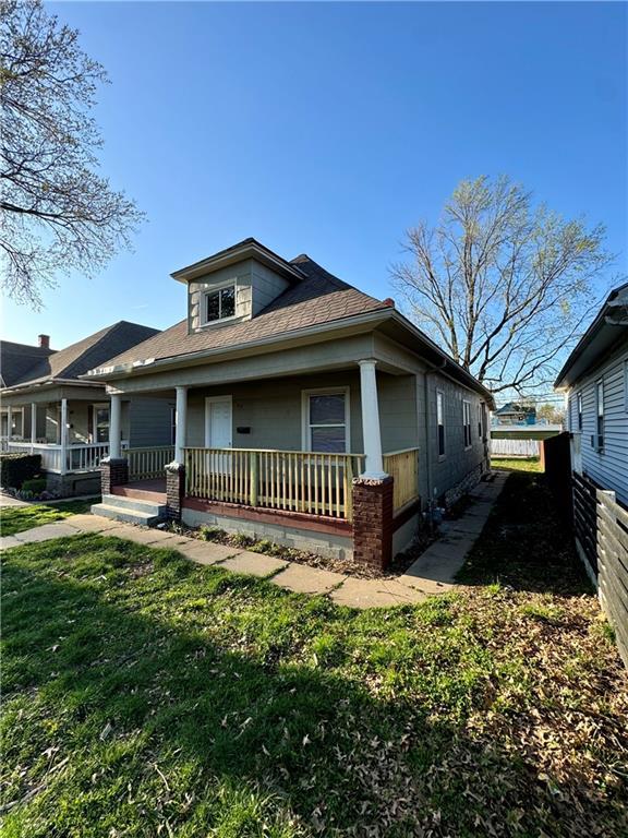 view of front of property with covered porch, a front yard, and fence