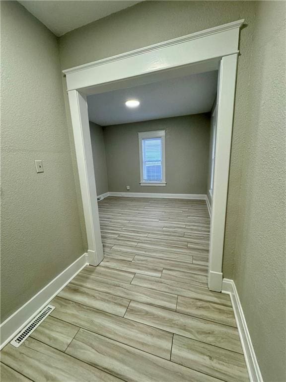 interior space featuring visible vents, baseboards, a textured wall, and wood tiled floor