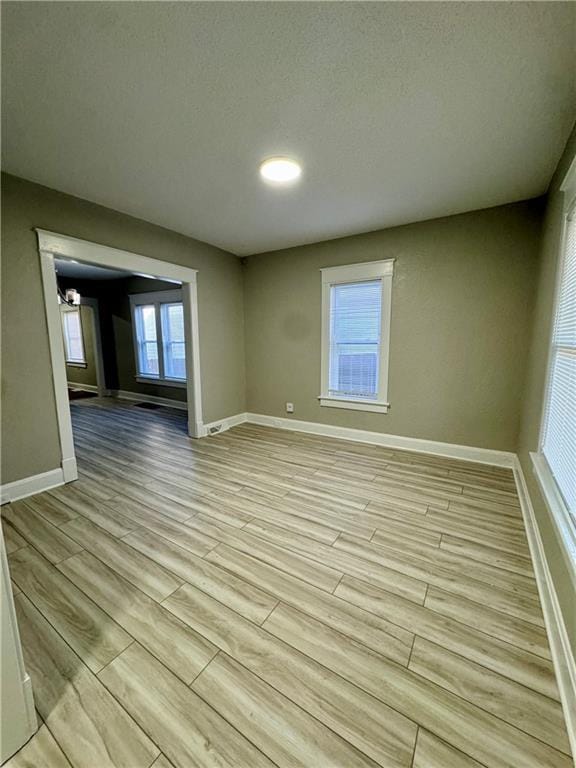 spare room featuring light wood-style floors, baseboards, and a textured ceiling